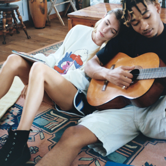 A girl leaning on a boy playing the guitar and sitting on the floor talking 