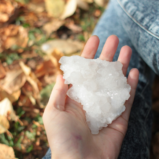 A hand holding a healing crystal selenite outside in nature