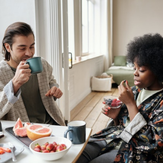 A woman eating fruit and a man drinking coffee as part of a morning ritual and aesthetic morning routine